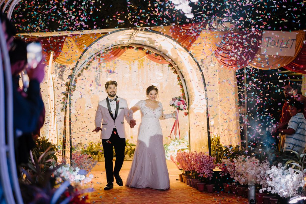Couple walks through illuminated archway during wedding celebration with confetti.