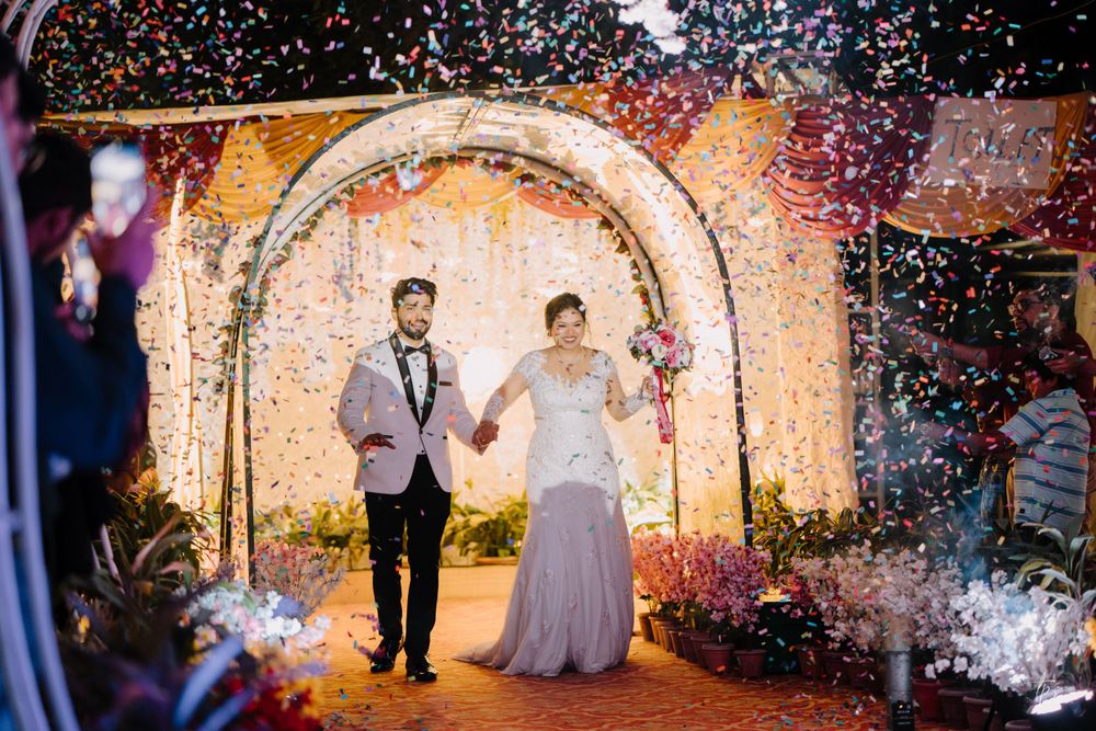 Newlyweds exit through floral arch as confetti rains down during celebration.