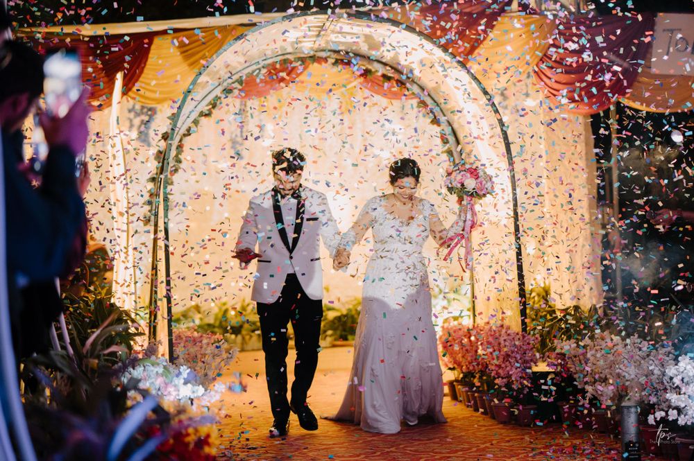 Wedding couple exits through decorated archway amid colorful confetti shower.