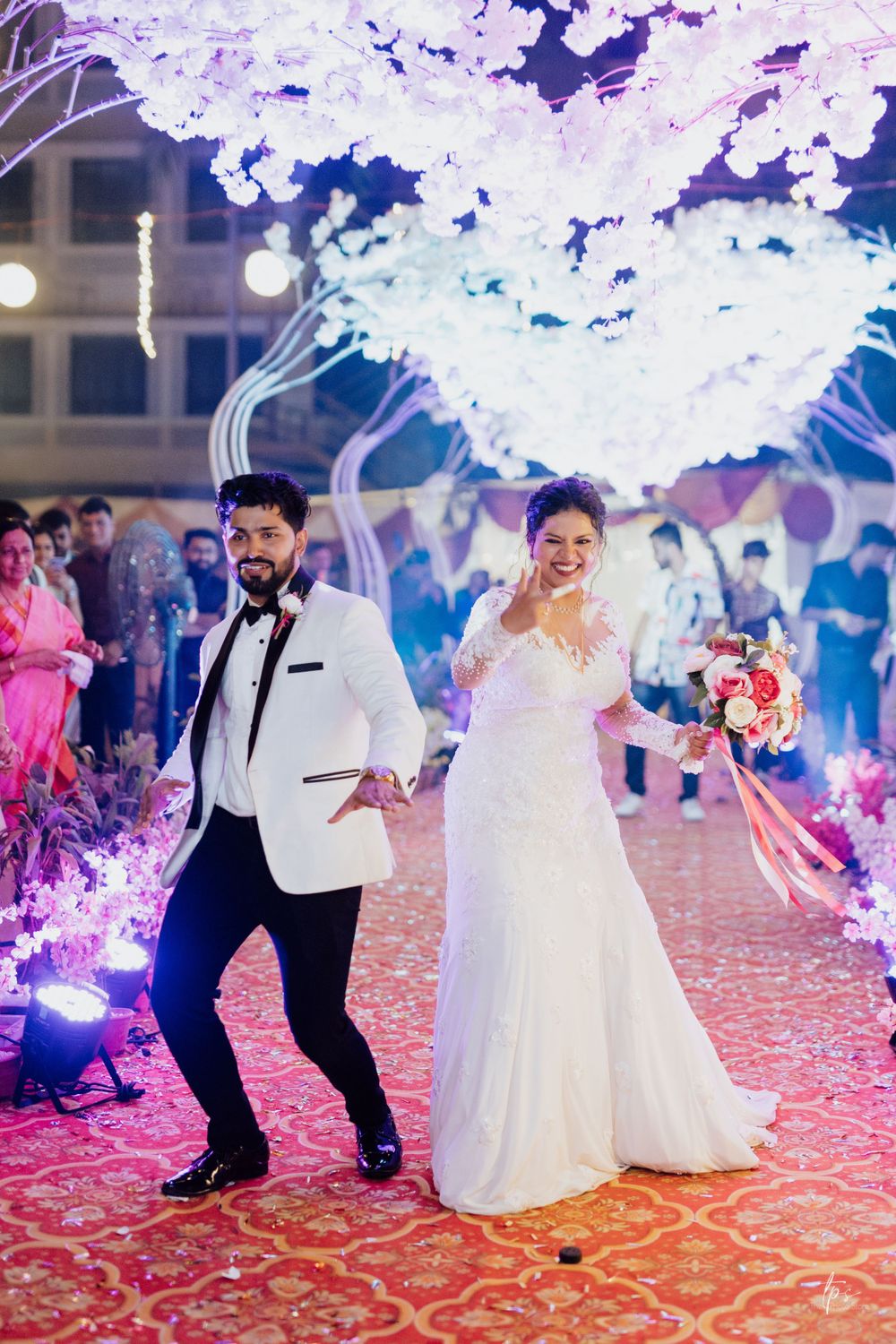 Couple dances energetically at their wedding reception under purple and white decorative lighting.