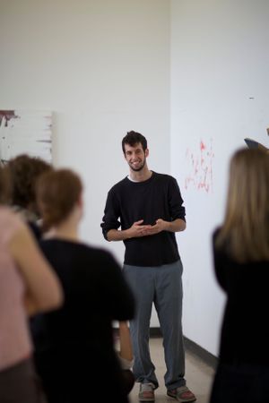 Person presenting to a small audience in a white-walled room.