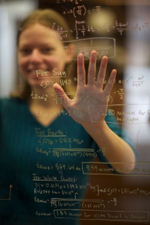 Student holds hand against glass with mathematical equations written on transparent surface.