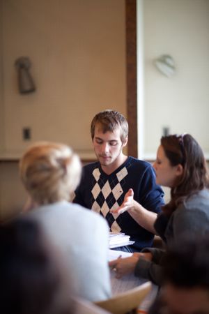 Students studying together at a table wearing argyle sweaters in a classroom setting.