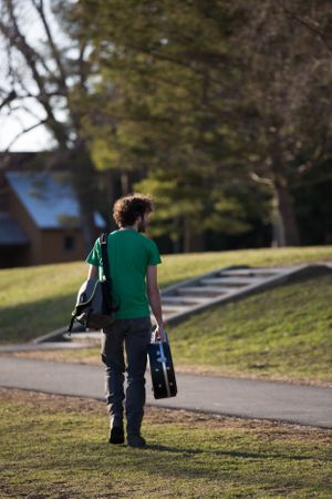 A person walking on a grassy path carrying a backpack on a sunny day.