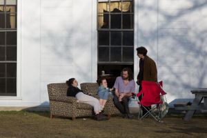 People relaxing outdoors on patio furniture against a white building with windows.