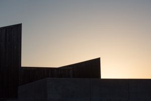 Minimalist architectural silhouette against a sunset sky showing geometric shapes and angles.