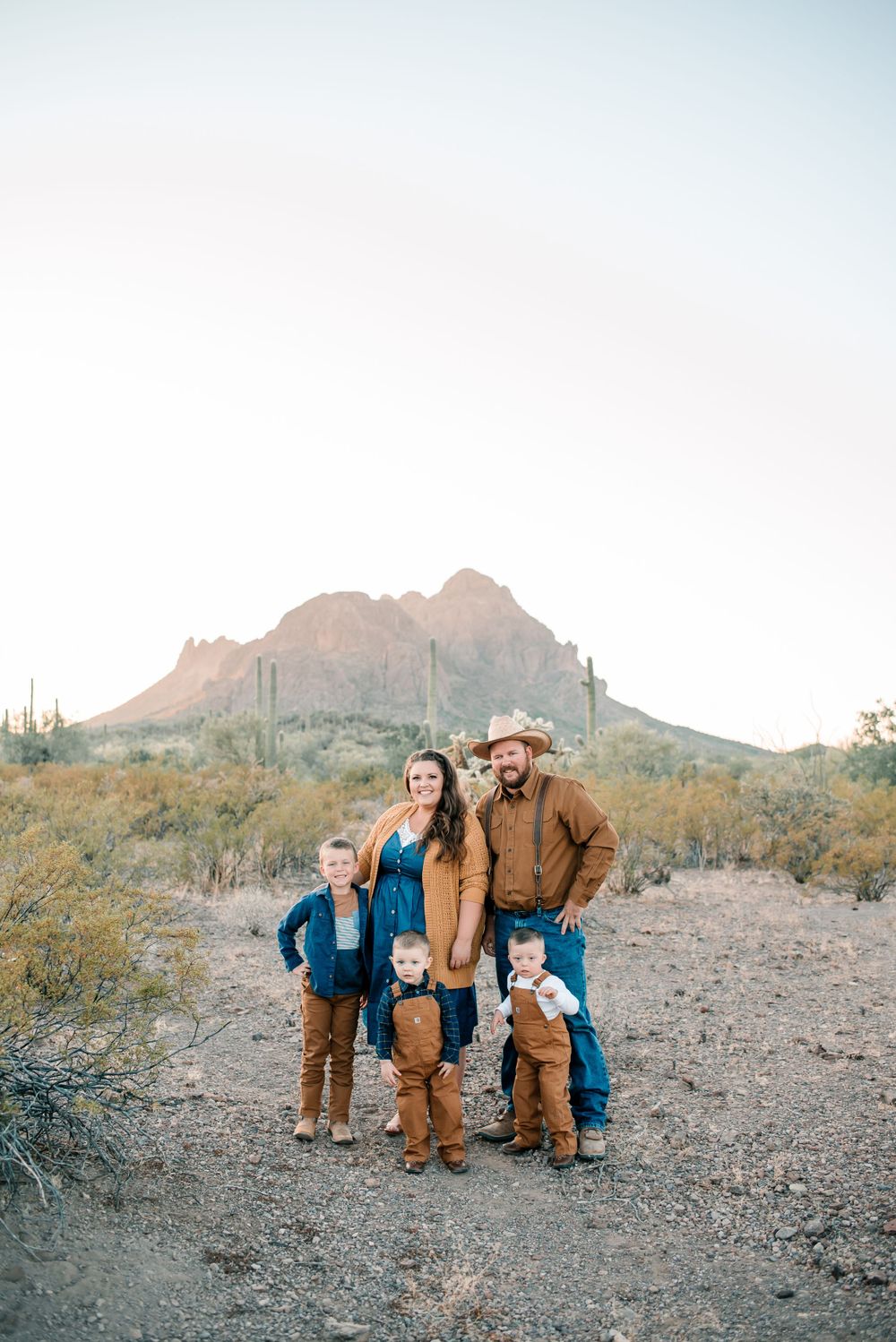 A family wearing matching brown outfits poses in front of desert mountains and saguaro cacti.
