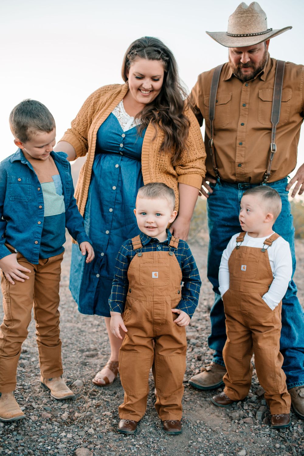 Family wearing matching workwear stands together on rocky desert ground with saguaro cactus visible.
