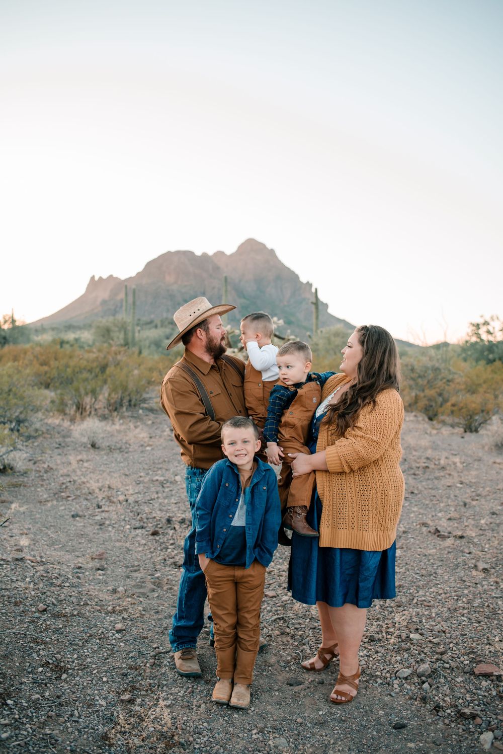 A family shares a tender moment against a desert mountain backdrop during golden hour.