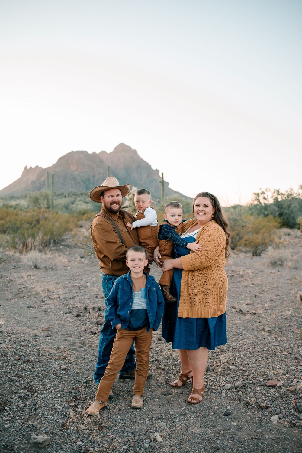 Family portrait in western attire with desert mountains and cacti creating a scenic backdrop.