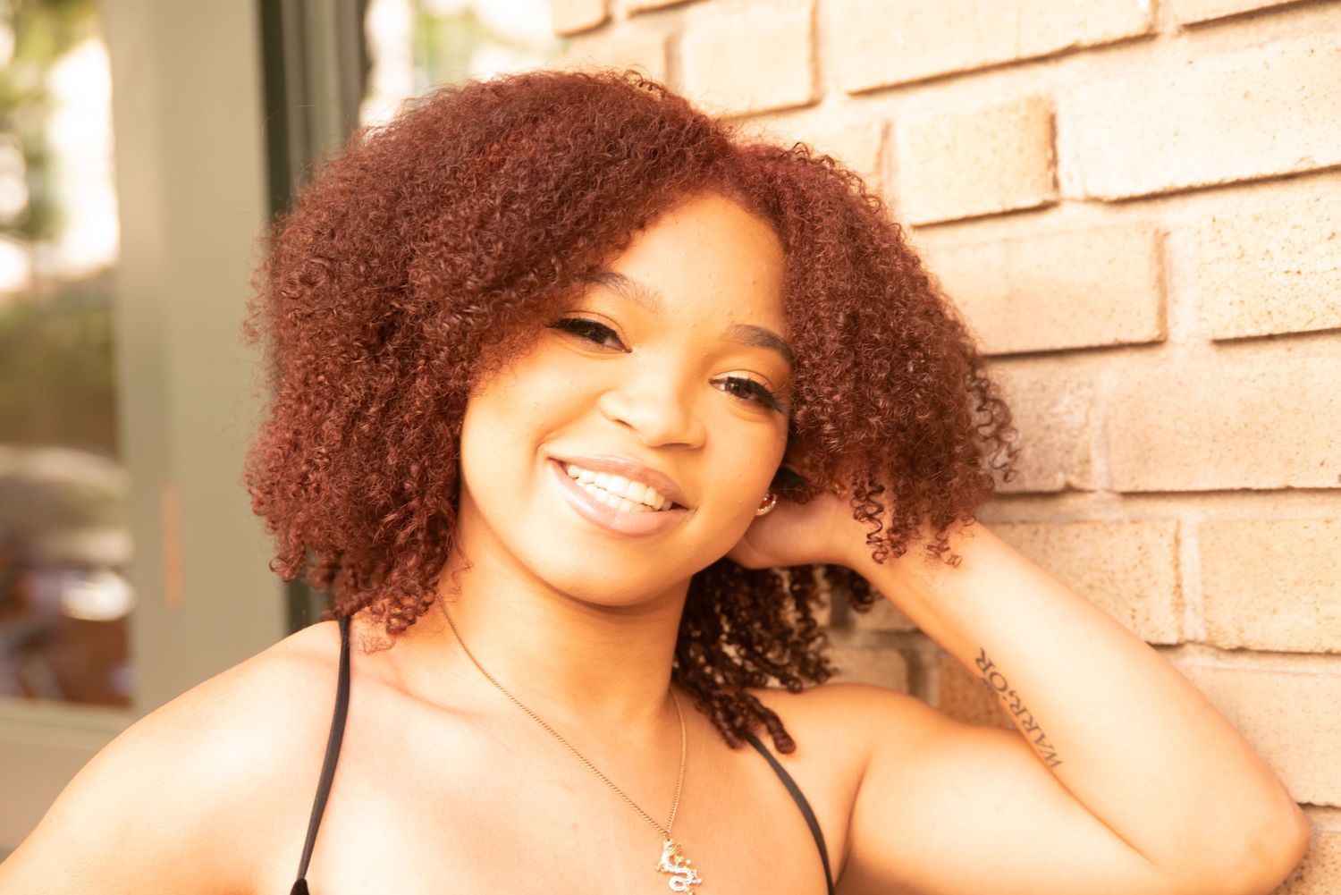 Graduate portrait with natural curly hair against brick wall background.