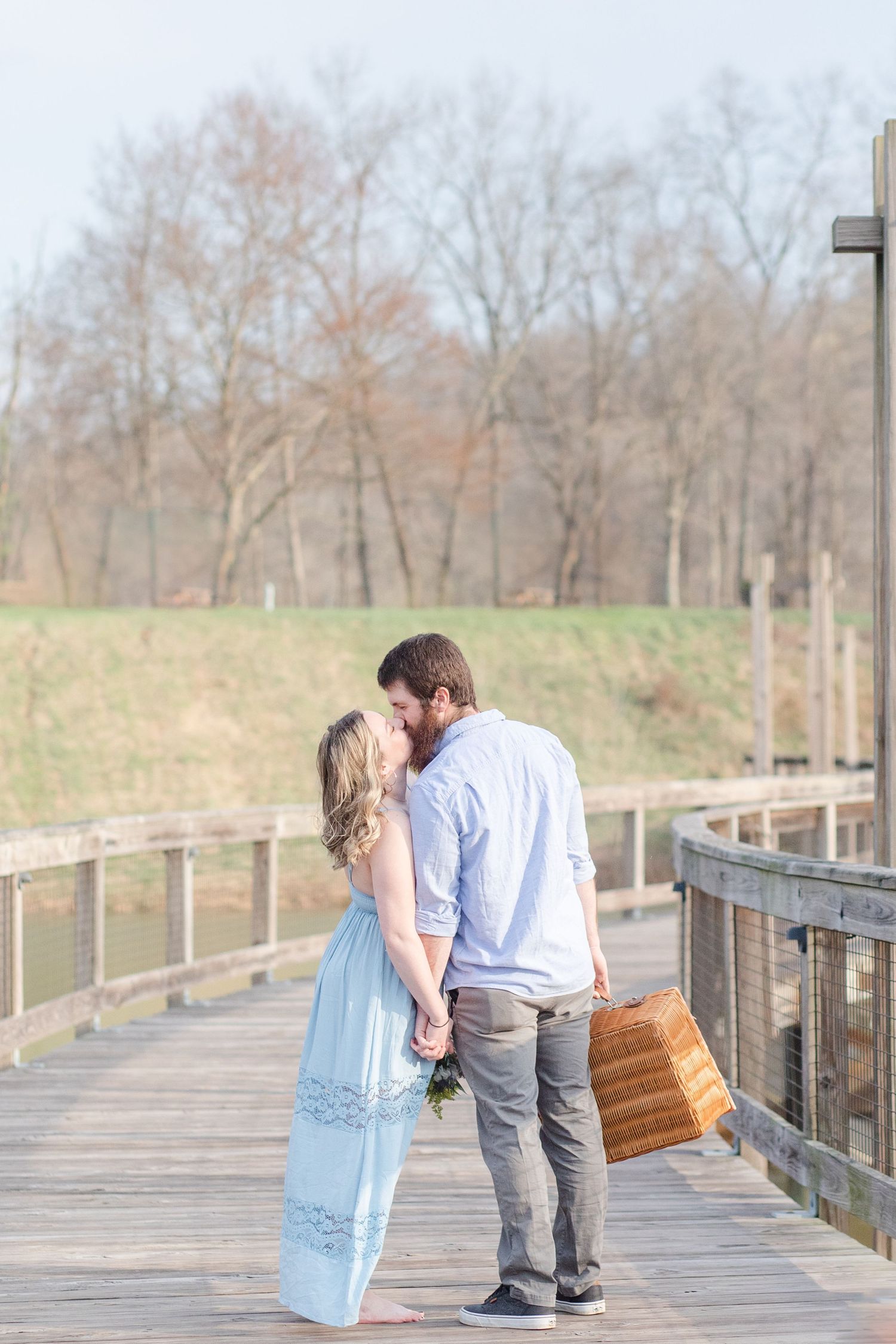 A couple walking along a wooden boardwalk carrying a picnic basket on a spring day.