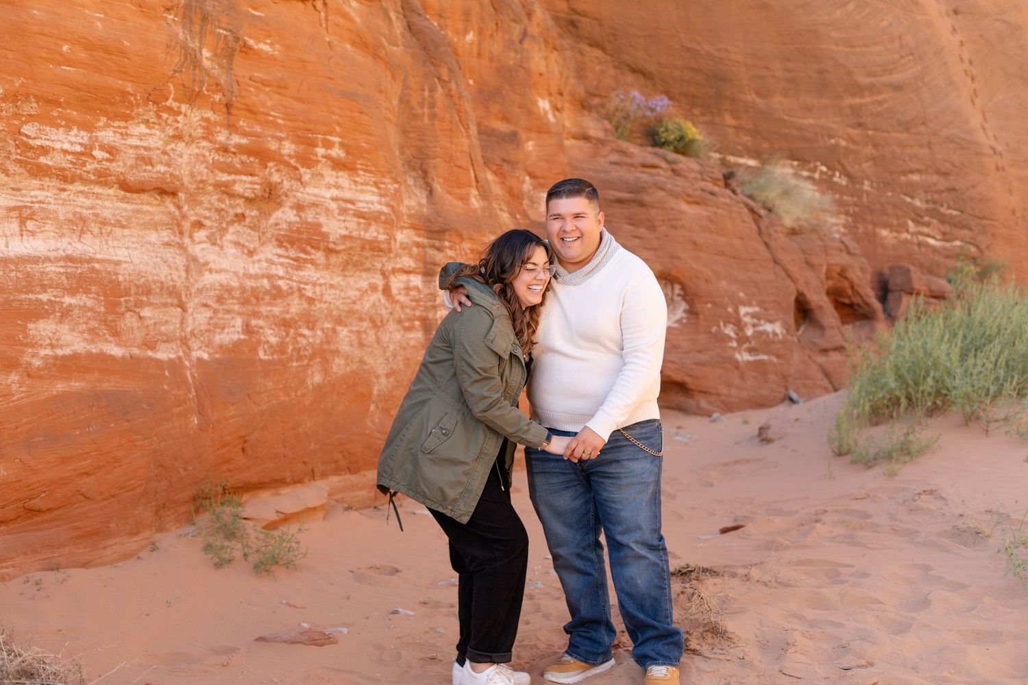 A couple stands together against red rock formations in a desert landscape.