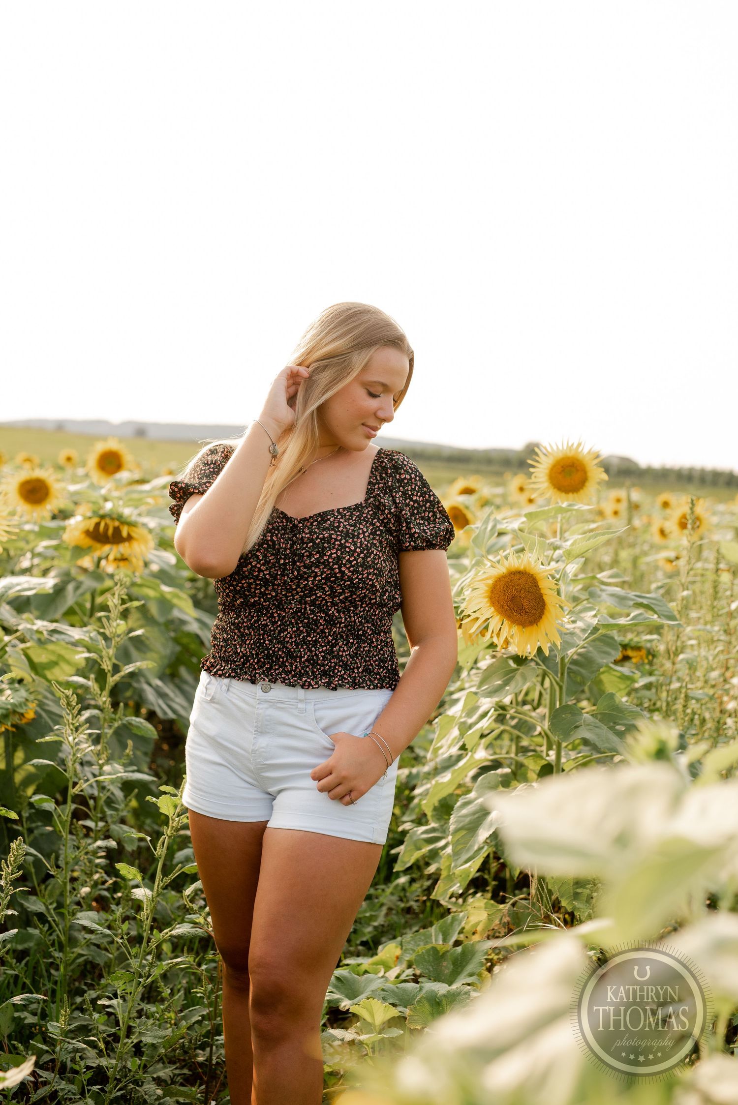 A casual summer portrait featuring a person in white shorts and patterned top amid sunflowers.