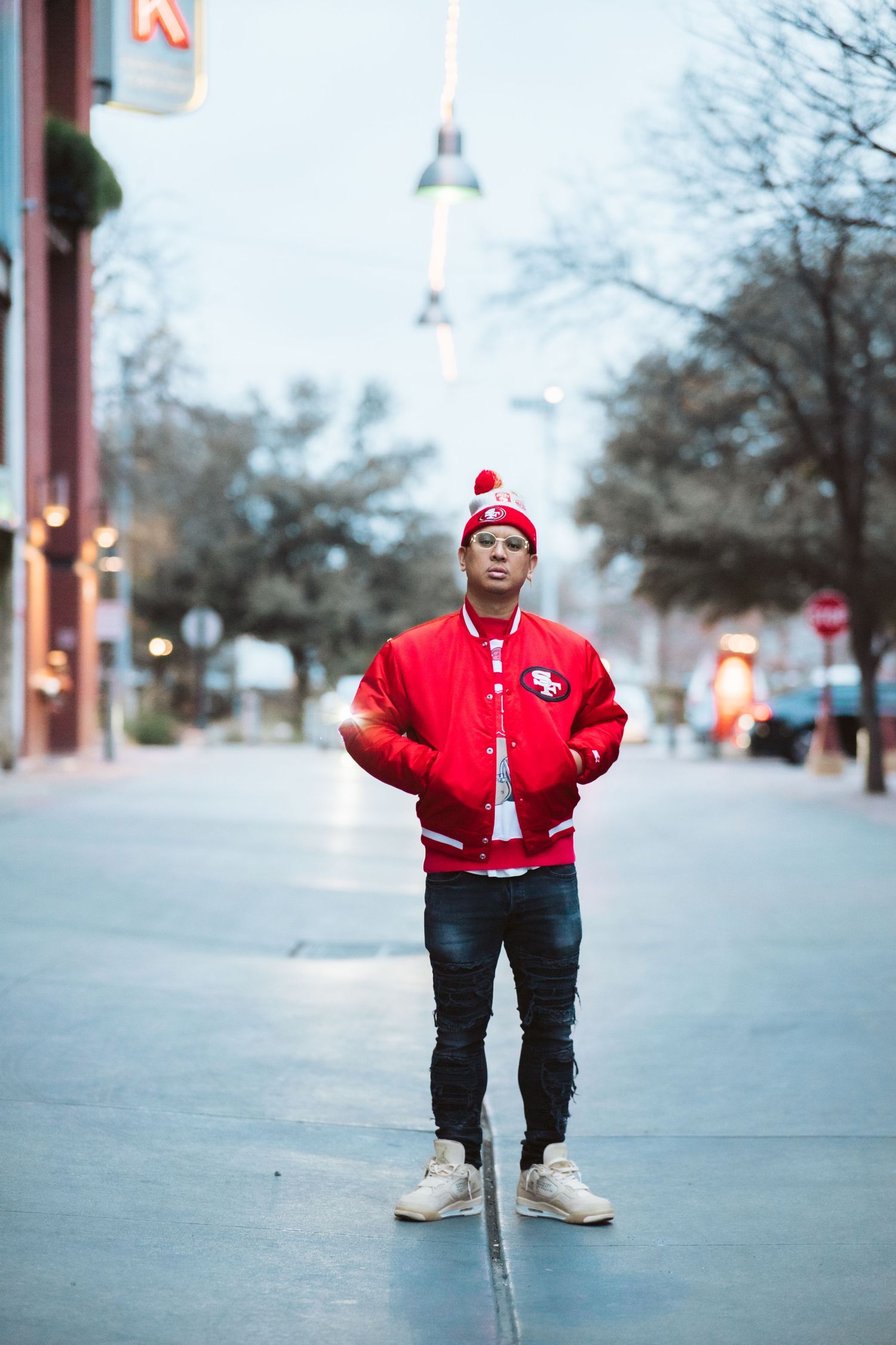 Person in red jacket and beanie standing on city street during blue hour.