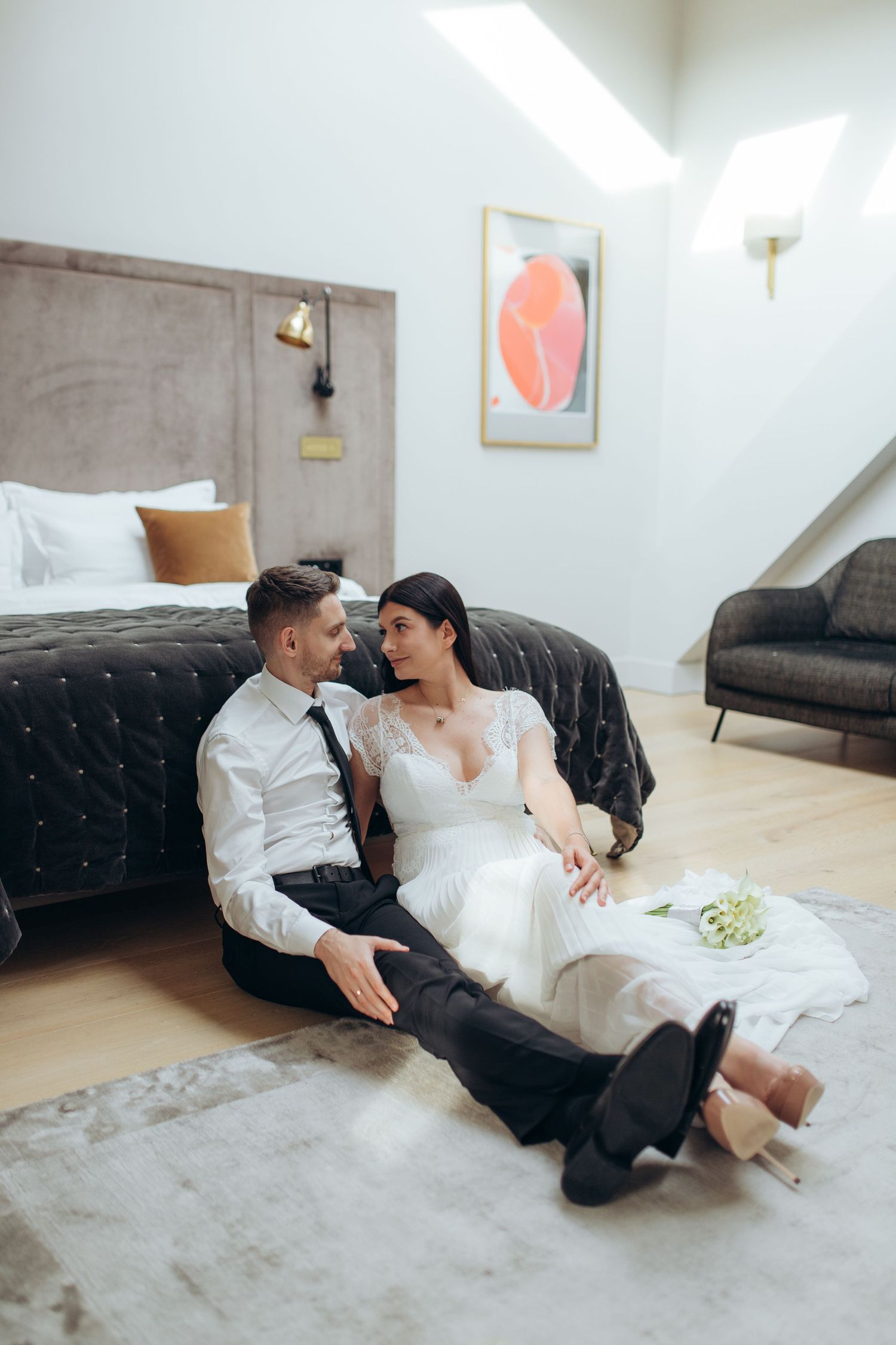 Romantic couple lounging together on floor next to bed in modern white bedroom with minimalist decor.