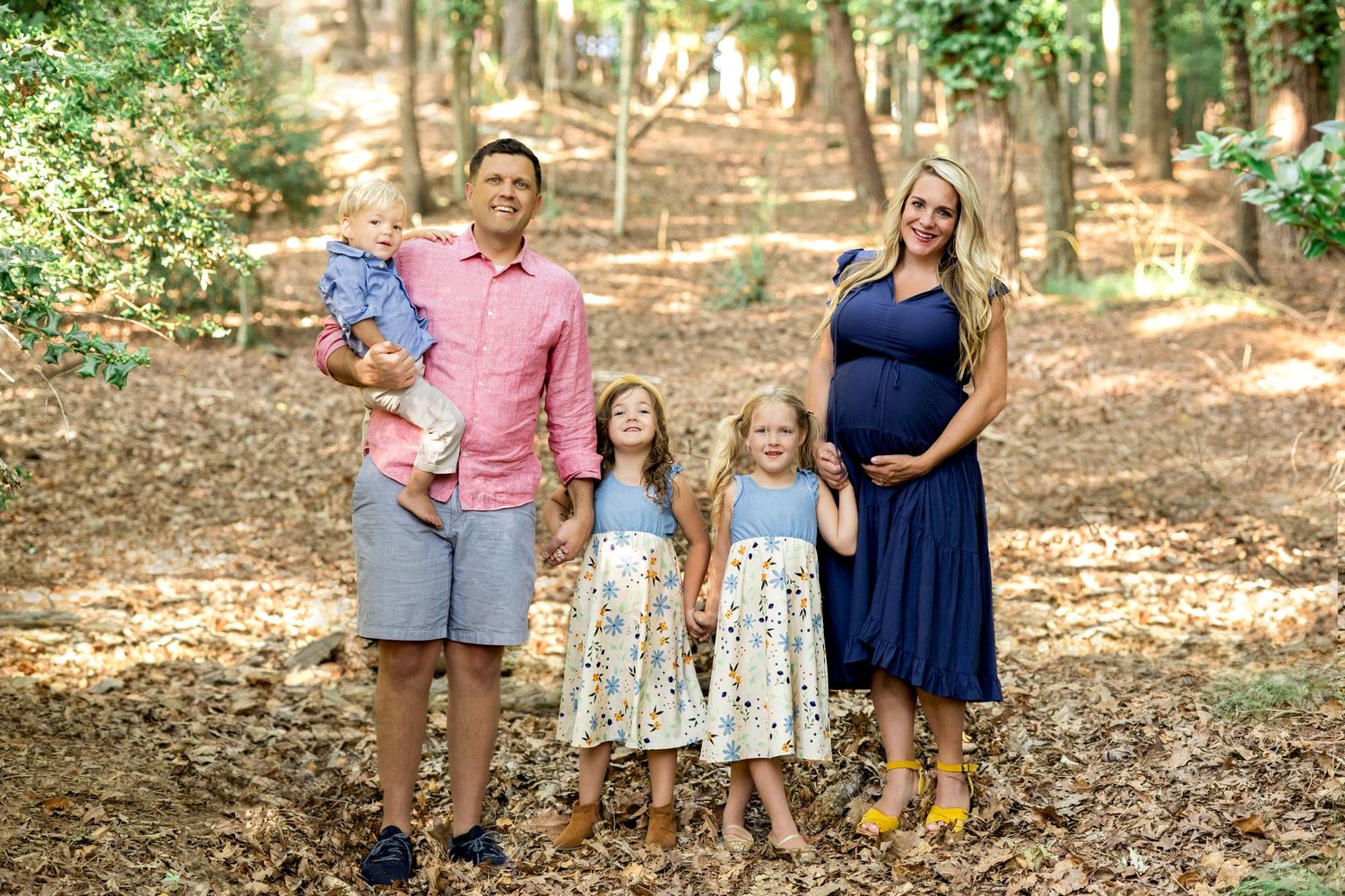 A family of four poses together on a wooded path during an outdoor photo session.
