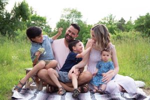 Family enjoying playful moment together on picnic blanket in summer meadow.