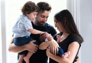 Family with toddler and newborn baby sharing tender moment together indoors.