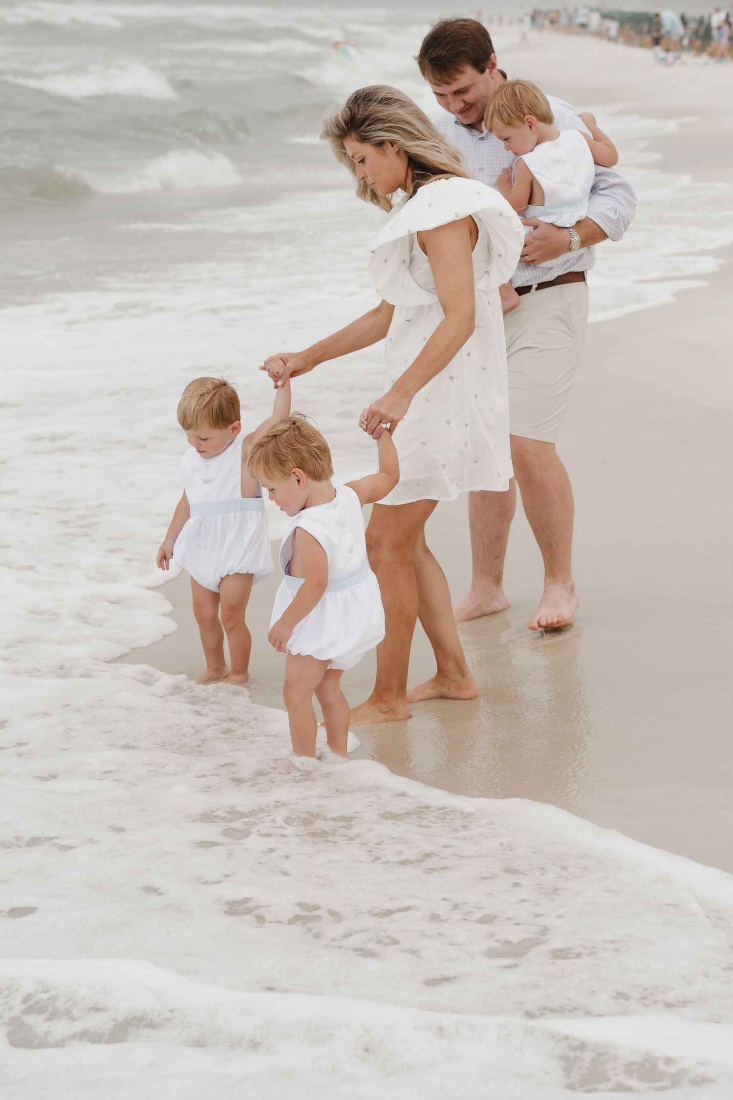 Family in white outfits playing together at the ocean's edge.