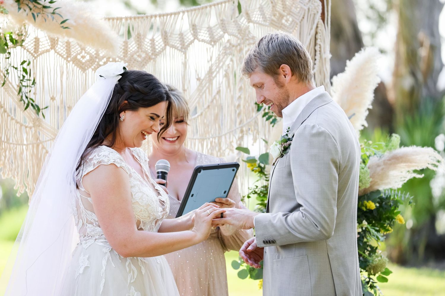 A romantic outdoor wedding ceremony under white decor where the couple exchanges vows using a tablet device.