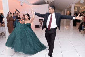 Two people dancing joyfully in formal wear on white marble floor.