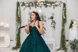Someone performs in an emerald green ballgown against a decorated white backdrop.