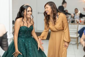 Two guests laughing together at a formal event, one in a sparkling emerald gown.