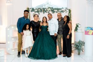 Group photo at formal event with woman in emerald green ball gown and floral decor in elegant white venue.