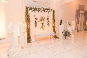 White event space decorated with hanging greenery, floral arrangements and illuminated number decor.
