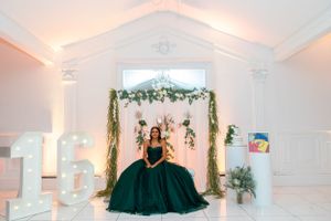 An emerald ballgown stands out against white decor and floral arrangements in an elegant venue.