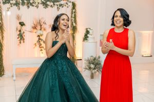 Two guests at a celebration posing in elegant formal dresses of emerald green and bright red against a floral backdrop.