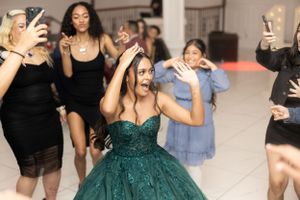 A group celebrating on the dance floor with a person in an emerald ballgown at the center.