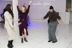 People dancing energetically on a white dance floor with purple accent lighting in the background.