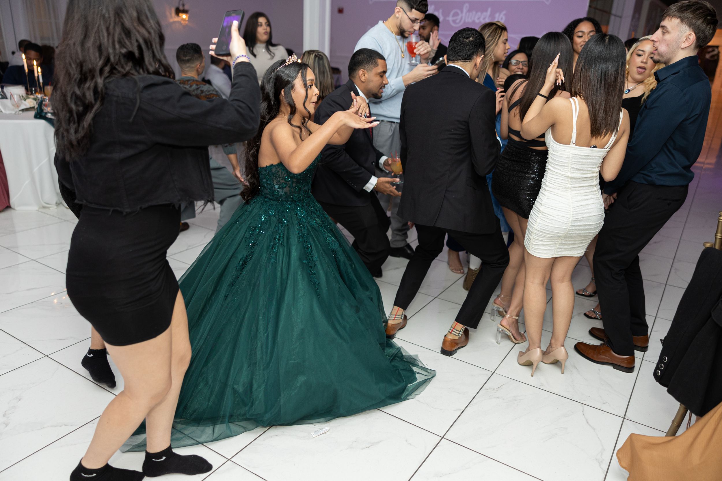 Guests dancing and celebrating on a white dance floor with someone wearing an elegant emerald ballgown.