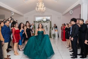 A celebration event with guests watching a performer in an emerald ballgown in an elegant white venue.