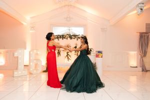 Person in red gown and another in emerald ballgown posing in elegant white venue.
