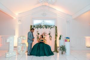 An elegant celebration venue with white columns, floral arch decorations and warm ambient lighting.