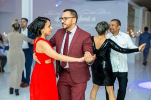 Couples dancing at formal event in elegant white venue with chandelier lighting.