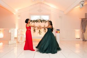 Two people in formal dresses sharing a moment in front of floral arch.