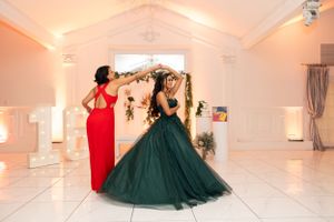 Person in red dress and another in emerald ballgown dancing together in elegant venue.