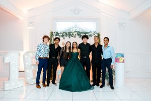 Three friends posing together against floral backdrop with one wearing an elegant emerald green gown.