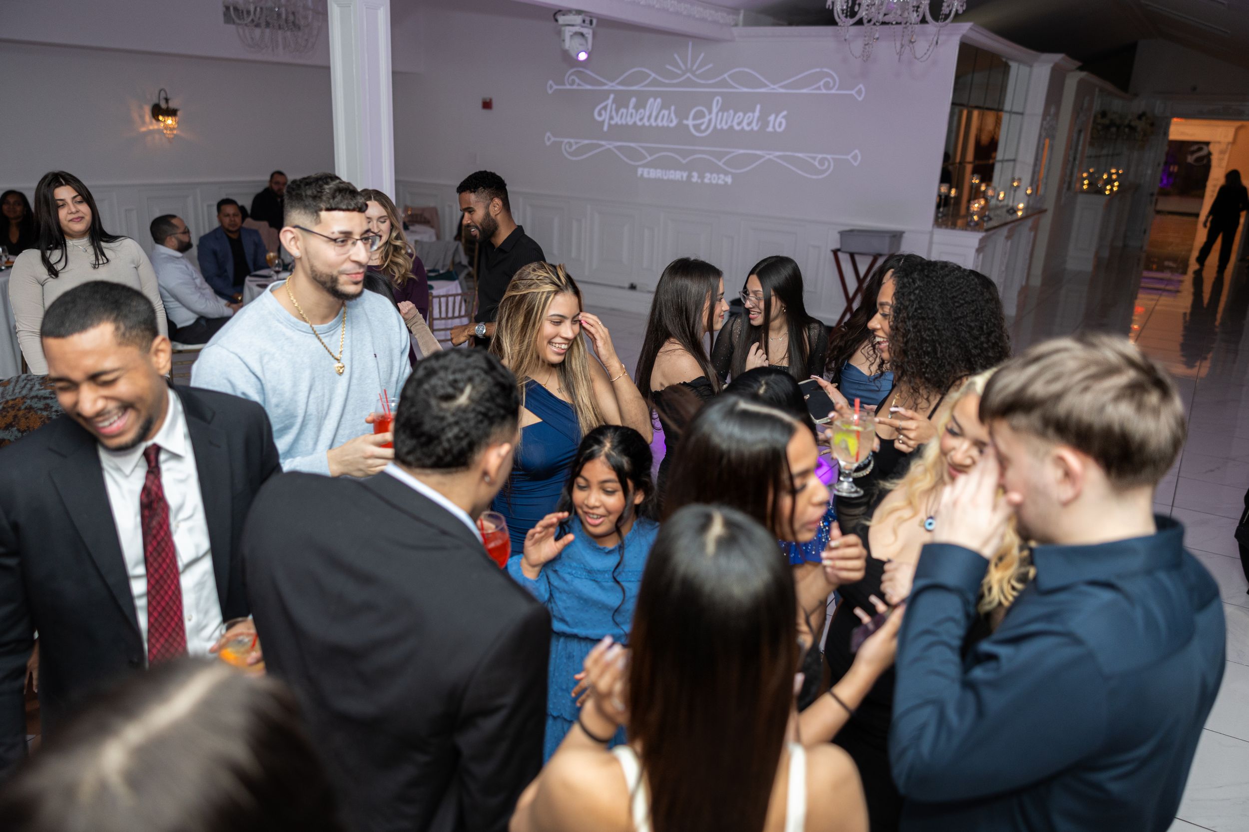 A crowded party scene showing guests mingling and dancing in an indoor venue.