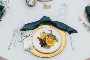 Formal place setting with emerald napkin, gold charger plate and plated meal.