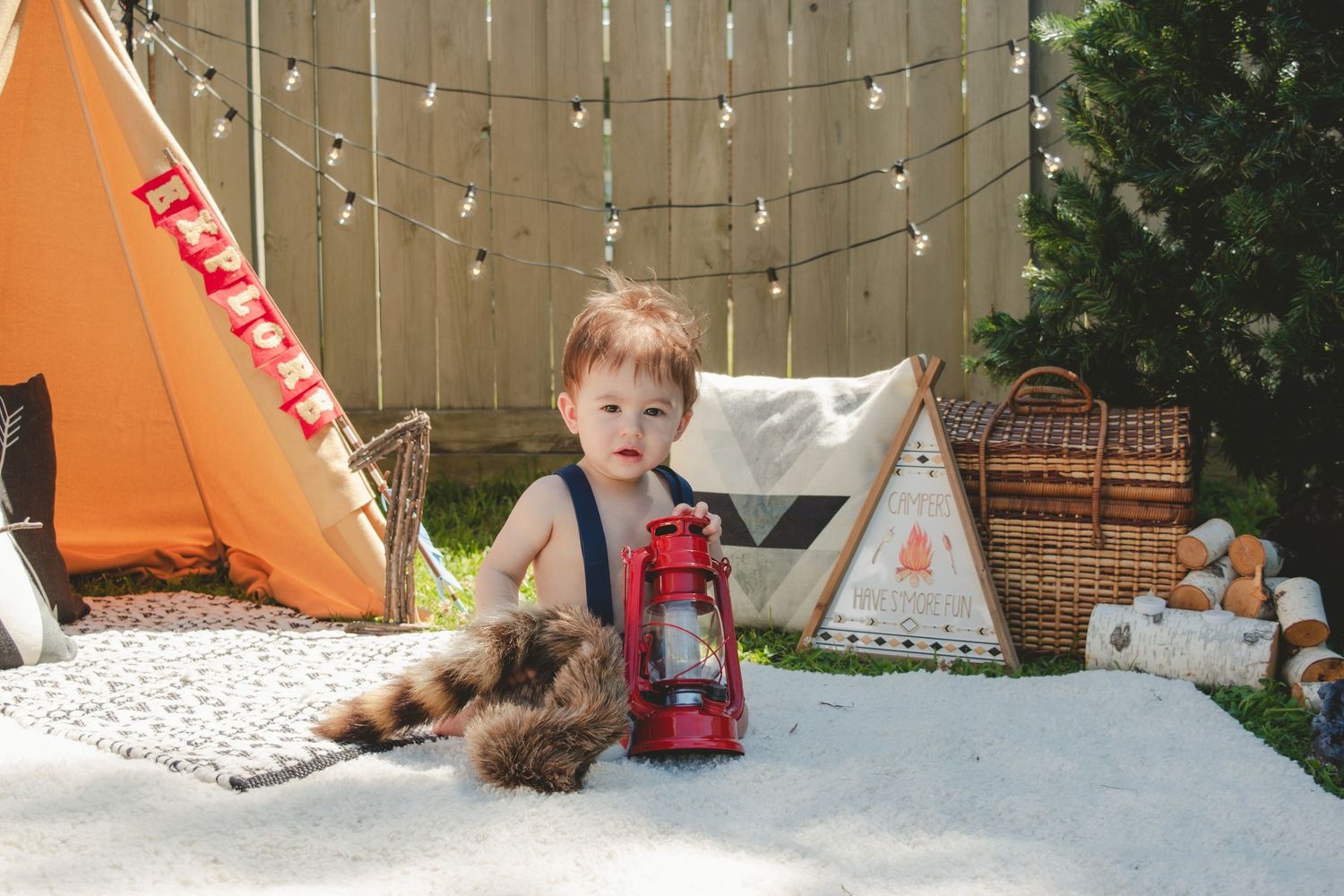 A camping-themed first birthday setup with teepee and vintage lantern decorations.