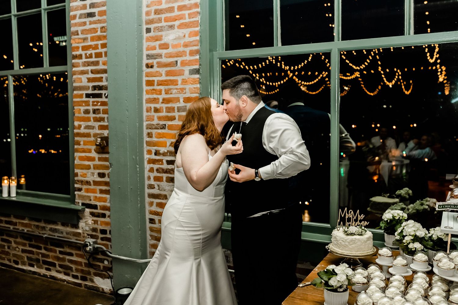 Indoor wedding reception with string lights and elegant decor against exposed brick walls.