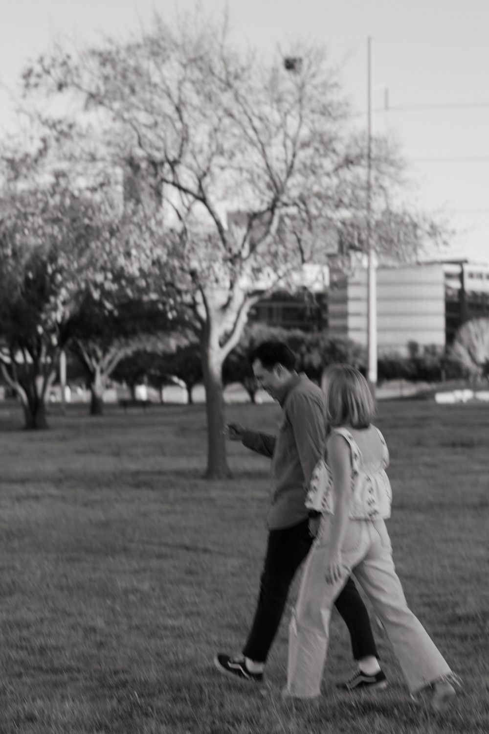Black-&-white of a trendy young couple walking in a downtown Fort Worth park during a couples photoshoot. She has ripped jeans & he has Vans