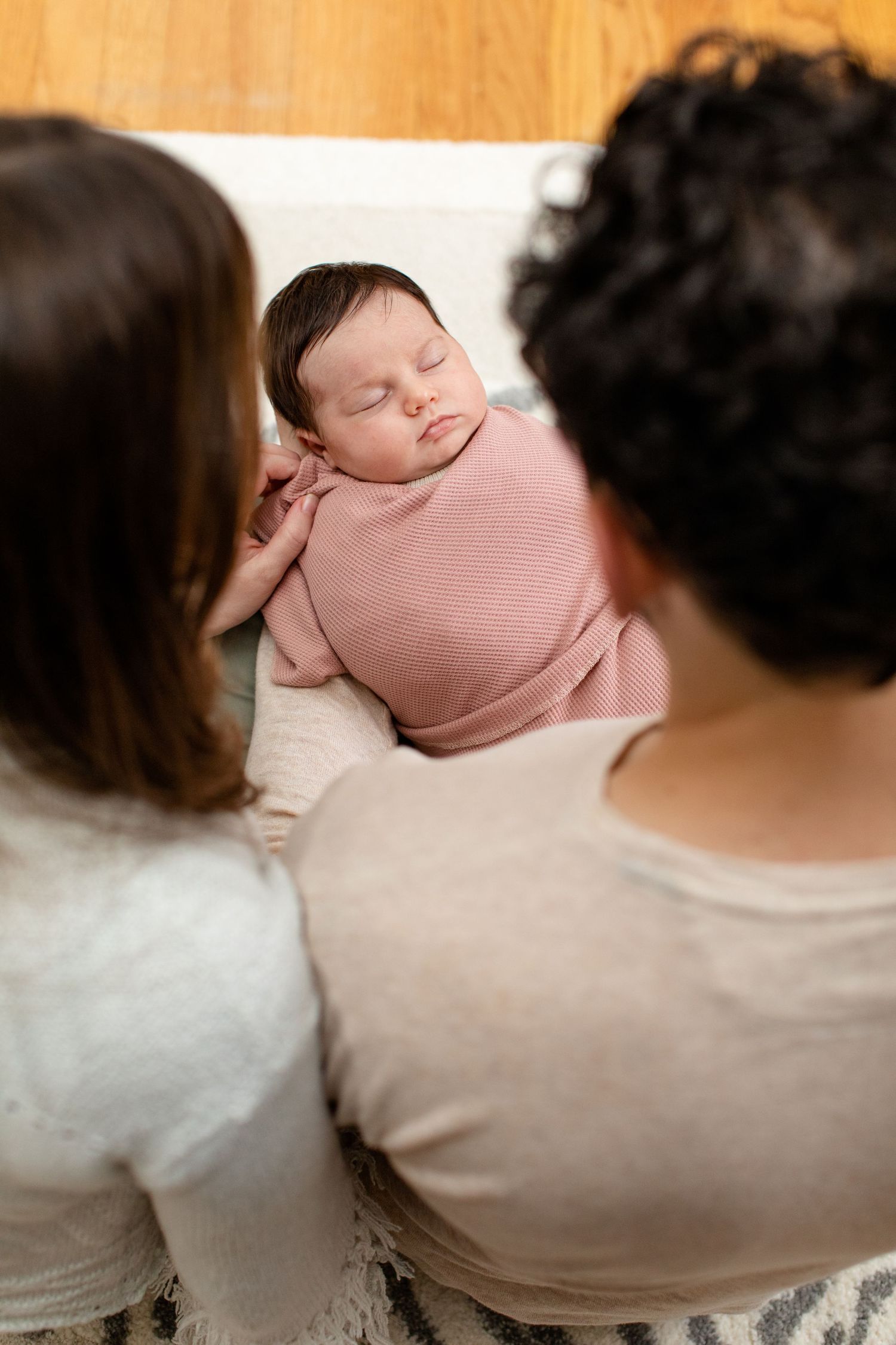 Sleeping newborn wrapped in pink swaddle viewed from over parents' shoulders.