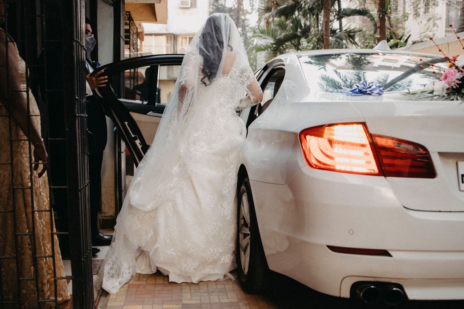 Wedding party approaching white luxury vehicle outside venue.