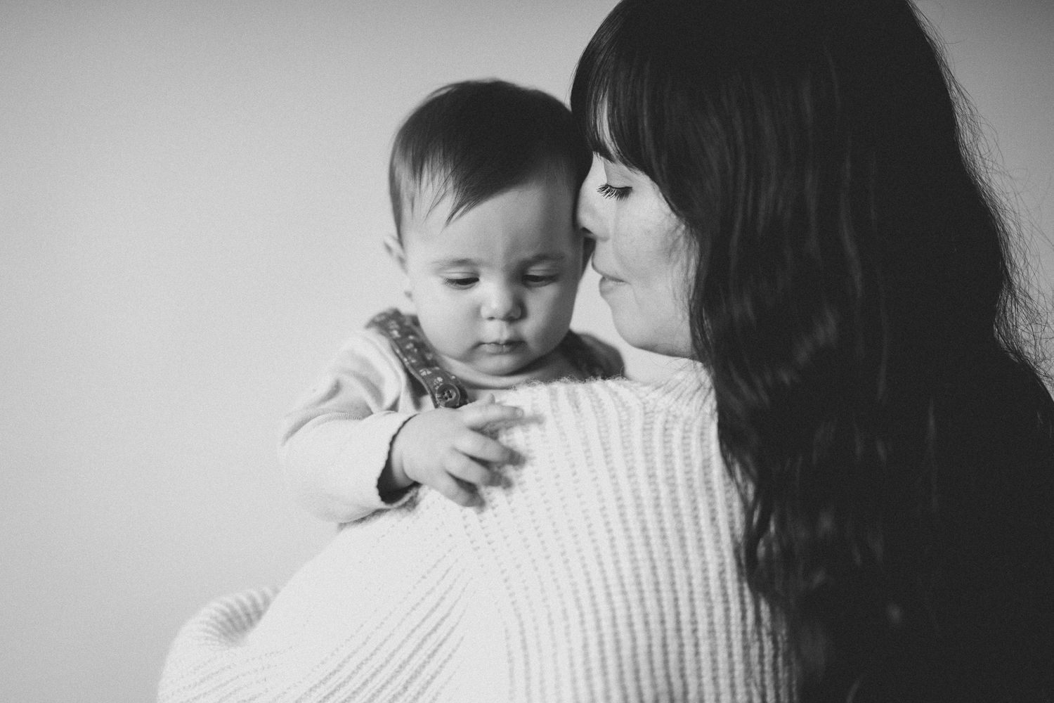 Tender moment between parent and baby in soft monochrome lighting.